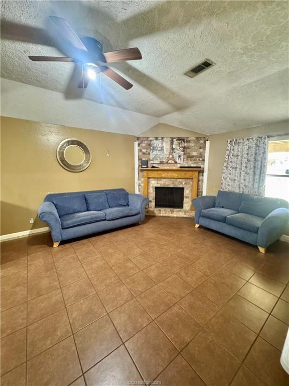 living area with a textured ceiling, visible vents, vaulted ceiling, a brick fireplace, and tile patterned floors