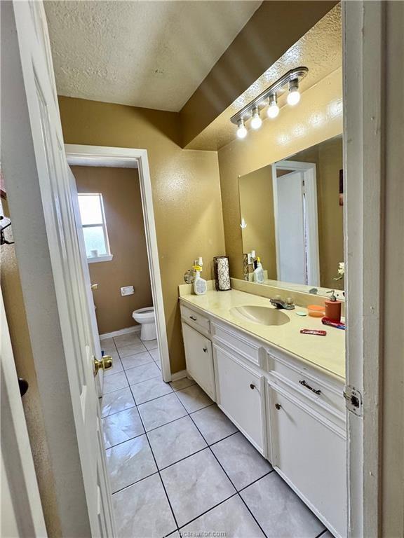 bathroom featuring toilet, vanity, a textured ceiling, baseboards, and tile patterned floors