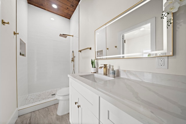 full bathroom featuring tiled shower, wooden ceiling, vanity, and toilet