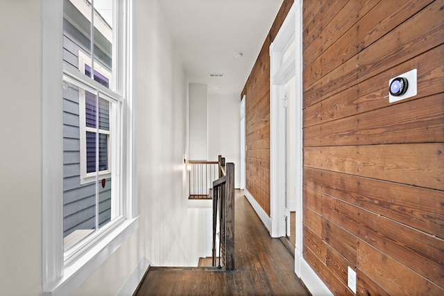 hall featuring baseboards, visible vents, wood finished floors, an upstairs landing, and wood walls