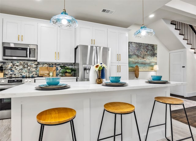 kitchen featuring appliances with stainless steel finishes, decorative backsplash, decorative light fixtures, and a kitchen breakfast bar