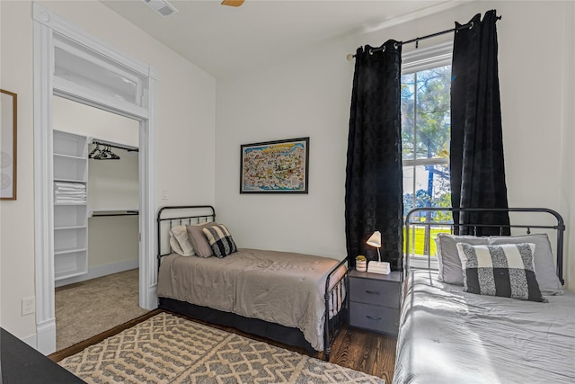 bedroom with a walk in closet, visible vents, baseboards, and wood finished floors