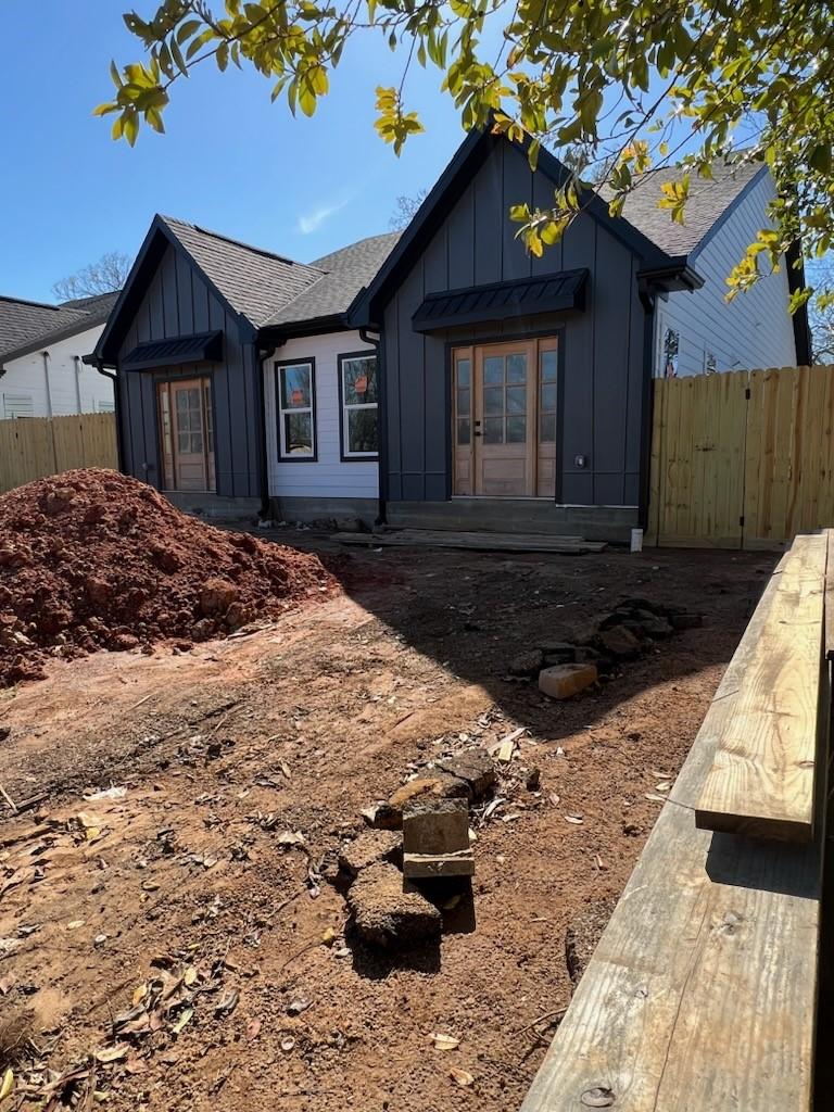 view of front of house with roof with shingles, french doors, board and batten siding, and fence