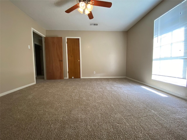 carpeted empty room featuring baseboards, visible vents, and ceiling fan