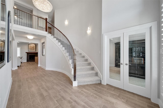 foyer entrance with stairway, a high ceiling, french doors, light wood-type flooring, and a fireplace