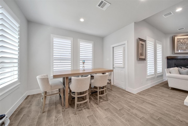 dining room with light wood-type flooring, visible vents, a fireplace, and baseboards