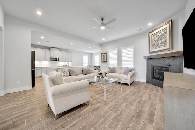 living area featuring a tile fireplace, light wood-style flooring, recessed lighting, visible vents, and baseboards