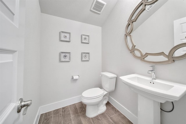 bathroom featuring toilet, baseboards, visible vents, and wood finish floors