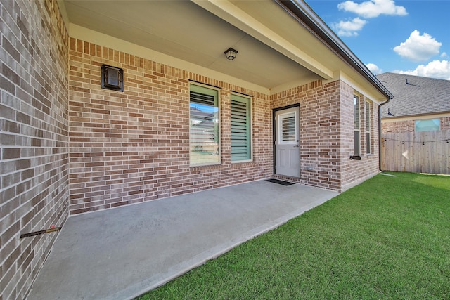 property entrance with a patio area, brick siding, a yard, and fence