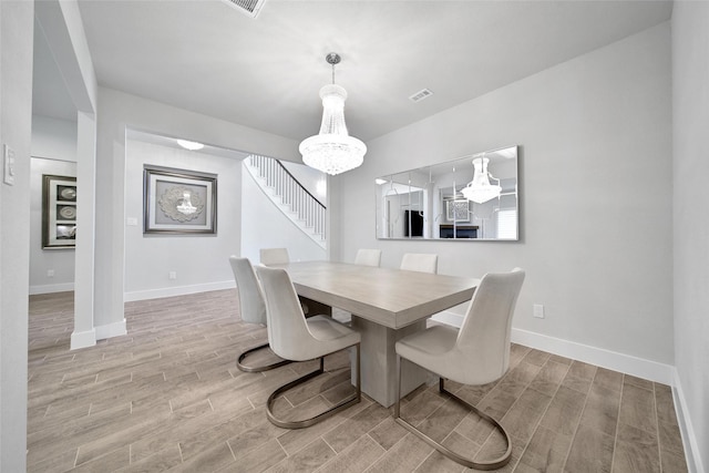 dining area with wood finish floors, visible vents, stairway, and an inviting chandelier