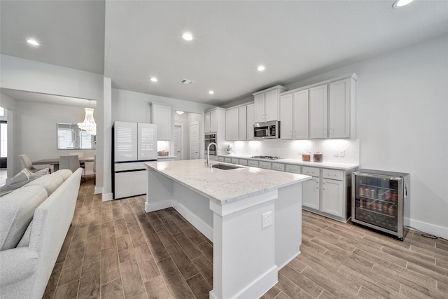 kitchen featuring beverage cooler, open floor plan, stainless steel appliances, light wood-type flooring, and a sink