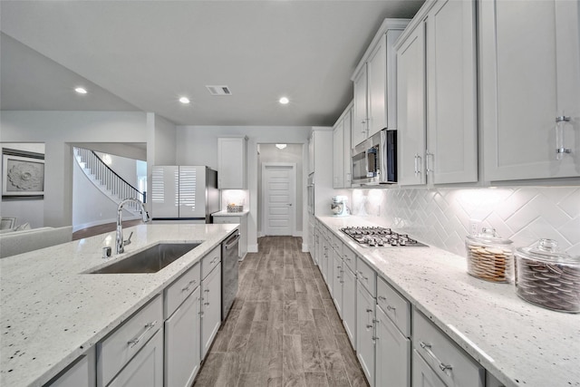 kitchen featuring stainless steel appliances, visible vents, backsplash, light wood-style flooring, and a sink