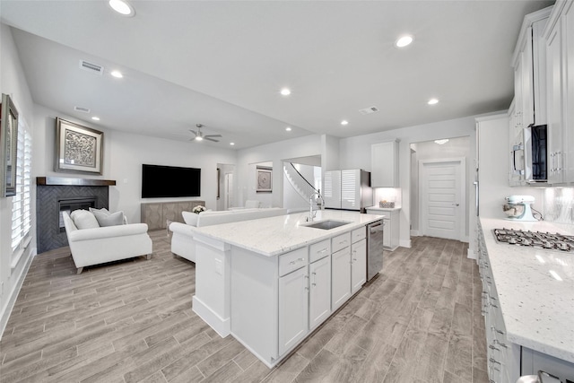 kitchen featuring recessed lighting, a sink, white cabinets, appliances with stainless steel finishes, and a glass covered fireplace