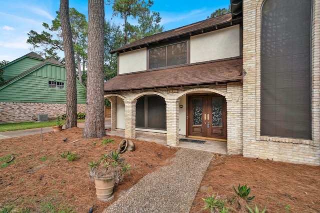 property entrance featuring a shingled roof, covered porch, brick siding, and stucco siding