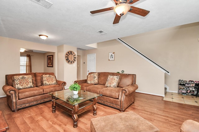 living room featuring a ceiling fan, visible vents, a textured ceiling, and light wood finished floors