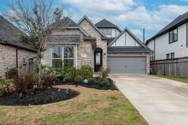 tudor house with a shingled roof, driveway, an attached garage, and fence