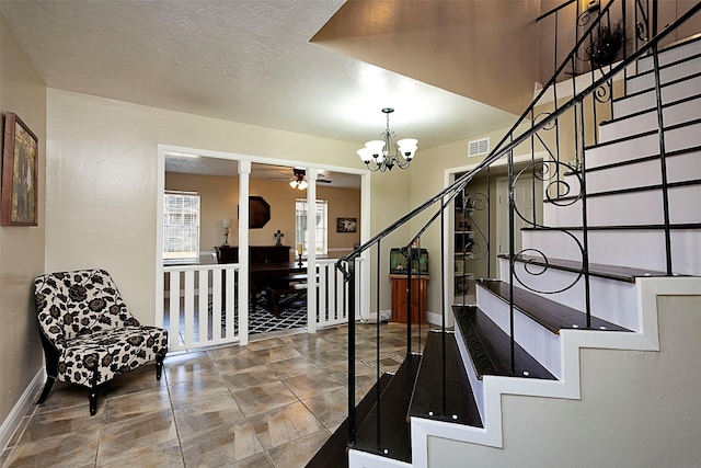 entryway with a textured ceiling, ceiling fan with notable chandelier, visible vents, baseboards, and stairway