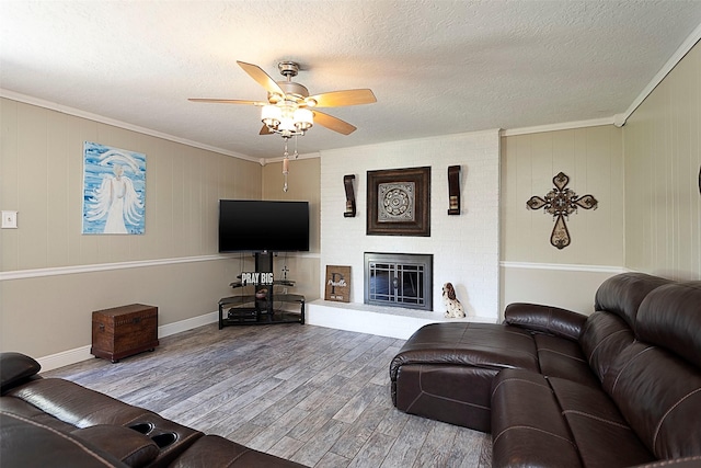 living area featuring a textured ceiling, a fireplace, wood finished floors, and crown molding