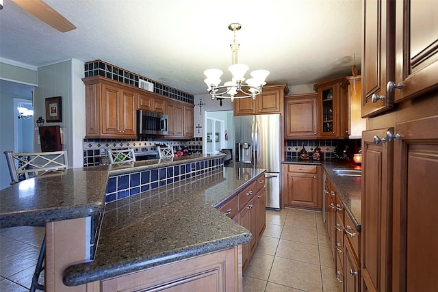 kitchen with a notable chandelier, backsplash, appliances with stainless steel finishes, brown cabinetry, and a kitchen island