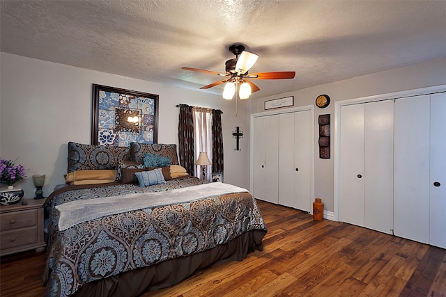 bedroom with a textured ceiling, two closets, hardwood / wood-style flooring, and a ceiling fan