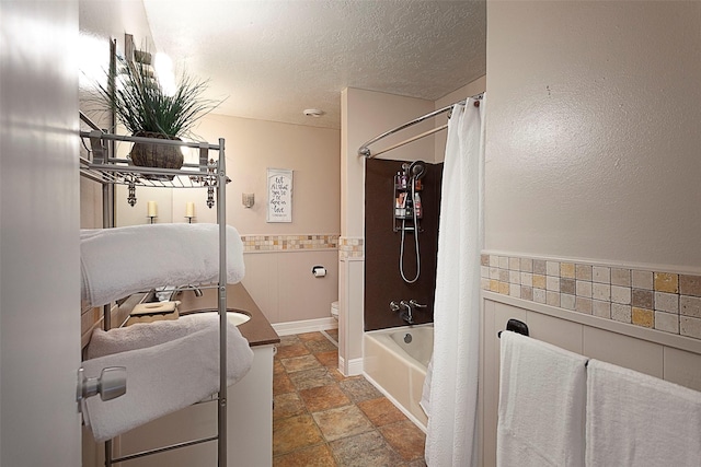 bathroom with a textured ceiling, toilet, a wainscoted wall, vanity, and stone finish floor