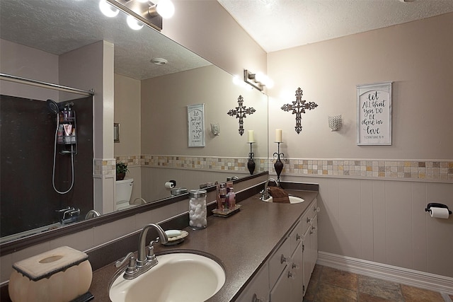 full bathroom with a textured ceiling, wainscoting, and a sink