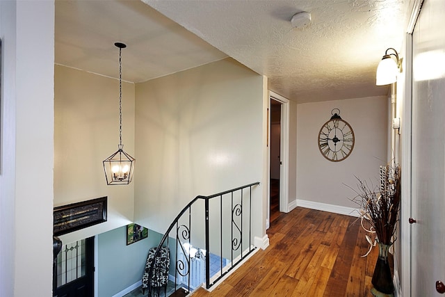 hall featuring a textured ceiling, a chandelier, hardwood / wood-style flooring, an upstairs landing, and baseboards