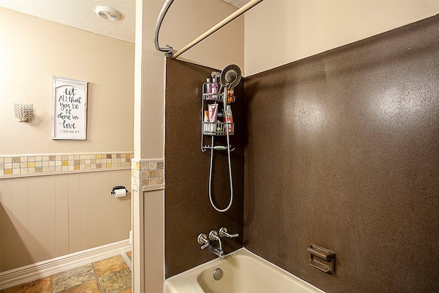 full bath with a textured ceiling, wainscoting, and bathtub / shower combination