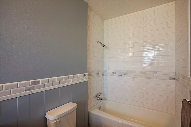 bathroom with a textured ceiling, wainscoting, shower / tub combination, and toilet