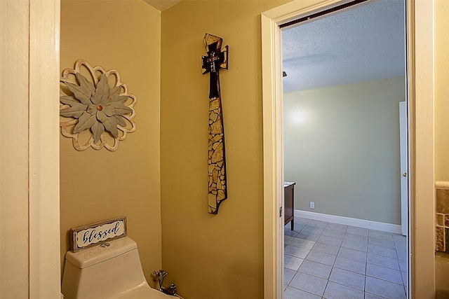 bathroom featuring baseboards, a textured ceiling, toilet, and tile patterned floors