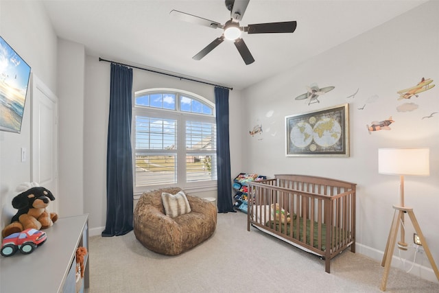 carpeted bedroom with ceiling fan, a crib, and baseboards