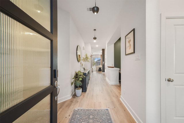 hallway with visible vents, light wood-style flooring, and baseboards