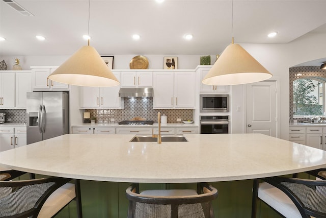 kitchen featuring backsplash, appliances with stainless steel finishes, white cabinetry, a sink, and under cabinet range hood