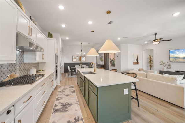 kitchen with stainless steel gas cooktop, a sink, white cabinetry, a kitchen bar, and green cabinetry