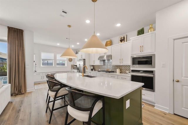 kitchen with tasteful backsplash, appliances with stainless steel finishes, light countertops, under cabinet range hood, and a sink