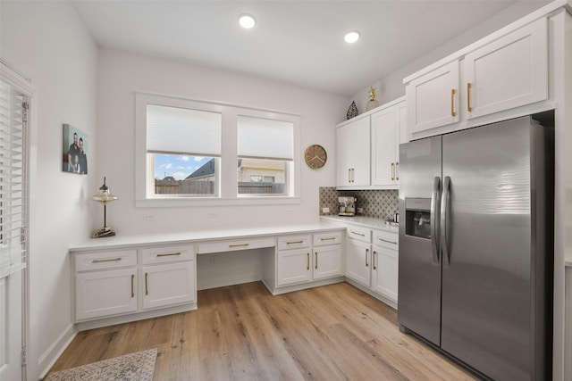 kitchen with built in desk, stainless steel refrigerator with ice dispenser, backsplash, white cabinets, and light wood-type flooring