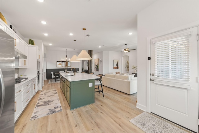 kitchen featuring a sink, white cabinetry, green cabinets, open floor plan, and a center island with sink