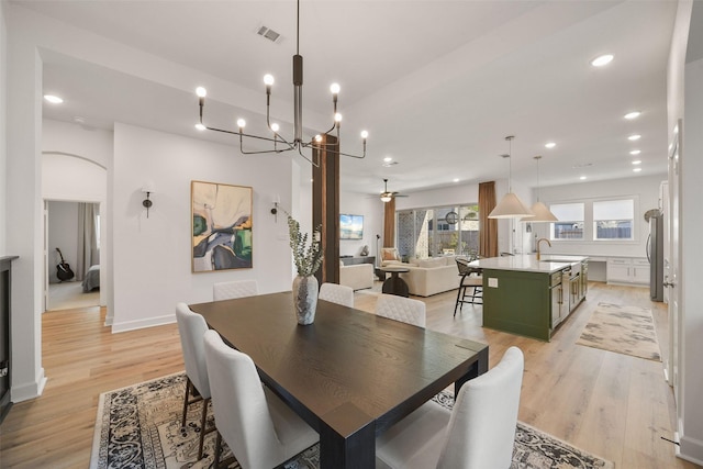 dining space with light wood-type flooring, visible vents, arched walkways, and a ceiling fan