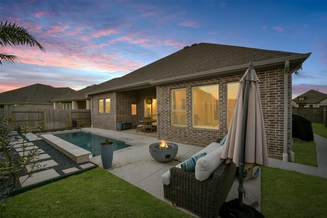 back of property at dusk with a patio area, brick siding, a fire pit, and a fenced backyard