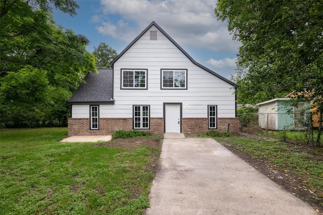 view of front of house with a shingled roof, a front yard, fence, and brick siding