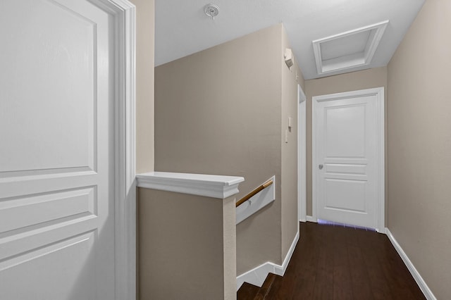 hall featuring attic access, baseboards, dark wood-type flooring, and an upstairs landing