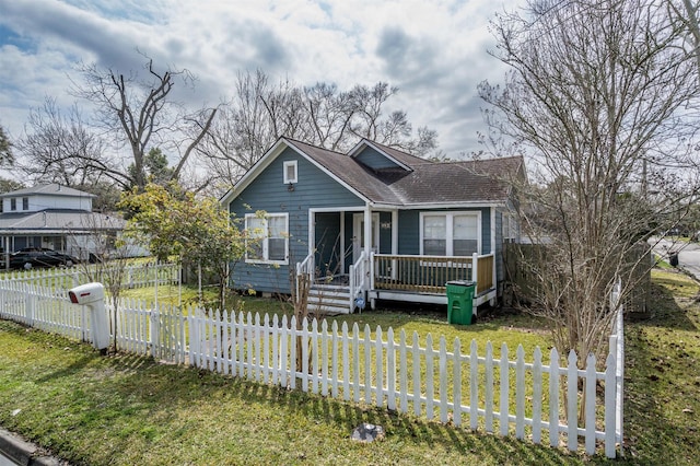 bungalow-style house with a shingled roof, a fenced front yard, and a front lawn