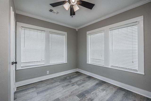 spare room with baseboards, visible vents, a ceiling fan, ornamental molding, and wood finished floors