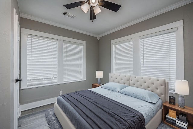 bedroom featuring ceiling fan, wood finished floors, visible vents, baseboards, and ornamental molding