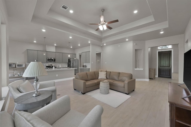 living room featuring light wood-type flooring, a raised ceiling, visible vents, and recessed lighting