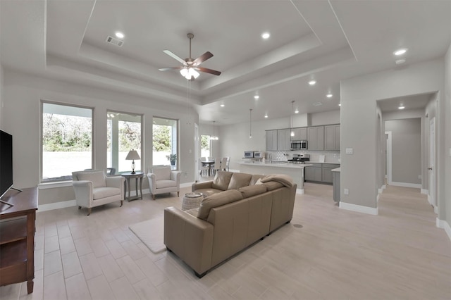 living room with a tray ceiling, plenty of natural light, visible vents, and baseboards