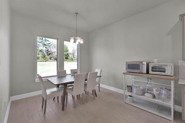 dining area with a toaster, light wood finished floors, baseboards, and a chandelier