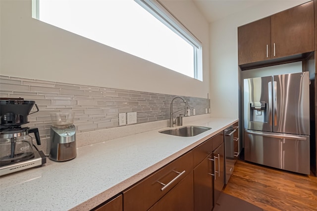 kitchen featuring stainless steel appliances, wood finished floors, backsplash, and a sink