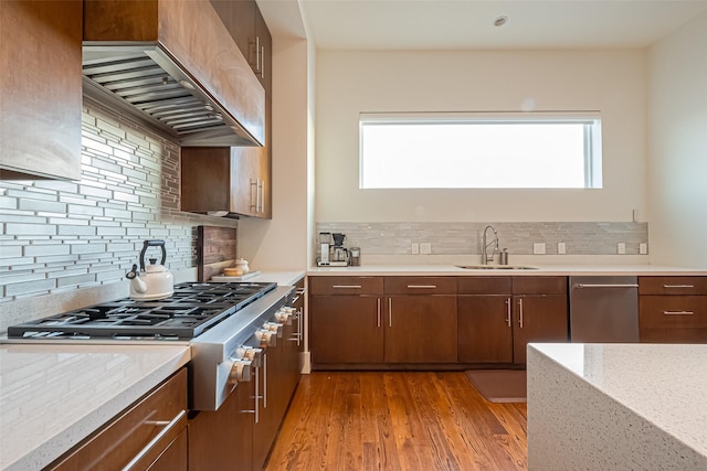 kitchen with light wood finished floors, stainless steel gas stovetop, a sink, wall chimney range hood, and plenty of natural light