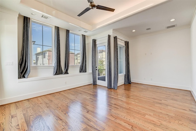 spare room featuring a raised ceiling, visible vents, light wood-style flooring, a ceiling fan, and baseboards